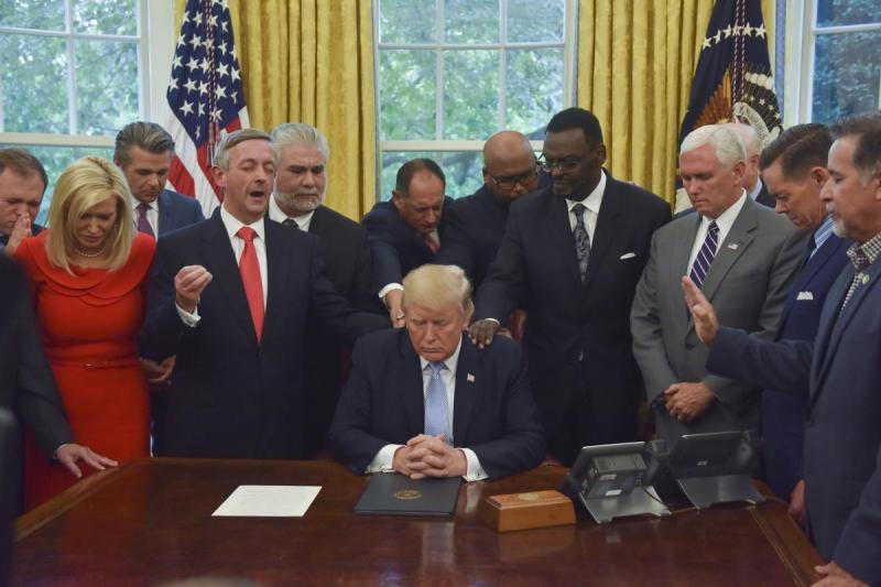 The photograph above is from a 2017 Oval Office meeting of religious right leaders "laying hands" on and praying for Trump. The picture has been featured in advertising by the Falkirk Center. The ad features text above the picture that reads, "Pray for Our President."